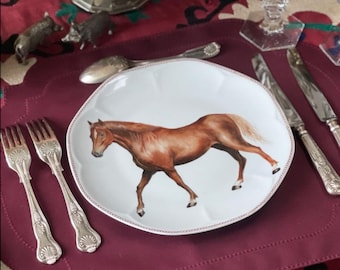May include: A decorative plate with a brown horse illustration. The plate is on a burgundy placemat, surrounded by silverware and a bouquet of pink roses. A gold pineapple candle holder and crystal glassware are also visible.