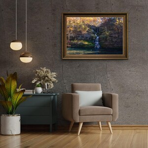 Puede incluir: Una fotograf&iacute;a enmarcada de una cascada que cae por un acantilado rocoso, rodeada de exuberante vegetaci&oacute;n verde y hojas de oto&ntilde;o. La fotograf&iacute;a est&aacute; colgada en una pared gris en un ambiente de sala de estar, con un sill&oacute;n marr&oacute;n y una mesa auxiliar con una planta en maceta.