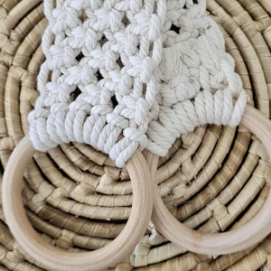 May include: Two wooden rings with a white crocheted rope attached. The rings are on a woven surface.