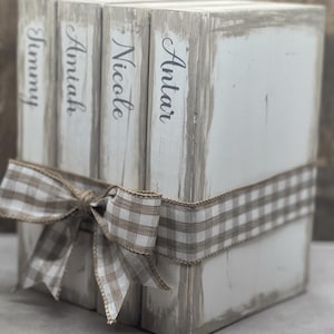 May include: Four white wooden boxes stacked on top of each other with a brown and white checkered ribbon tied around them. The boxes are labeled with the names "Antari", "Nicole", "Amiah", and "Jimmy".