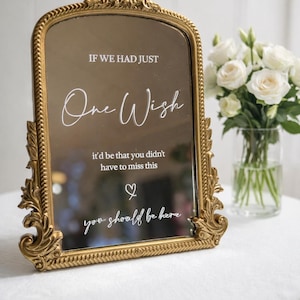 May include: A gold-framed mirror with ornate detailing. The mirror reflects the surroundings and features the text "IF WE HAD JUST One Wish...you should be here." A vase of white roses sits nearby, suggesting a wedding or special event.