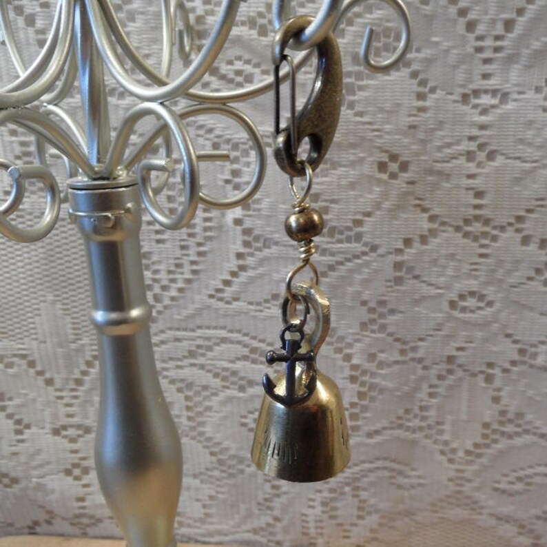 May include: A gold-toned bell charm with an anchor pendant. The charm is attached to a silver-toned safety pin.