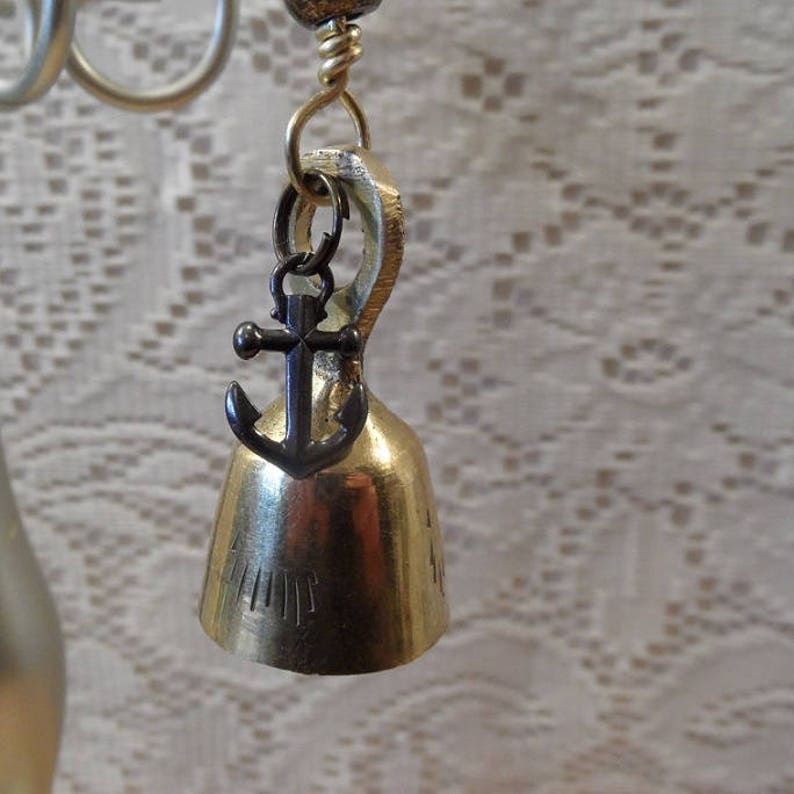 May include: A gold-colored bell with an anchor charm hanging from it. The bell has a small inscription on the side.