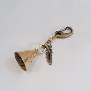 May include: A brass bell keychain with a small feather charm and a brass clasp.