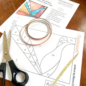 May include: A stained glass pattern for a roadrunner design. The pattern is printed on white paper and includes numbered pieces. The pattern is accompanied by copper tape, scissors, and a tool for cutting glass.