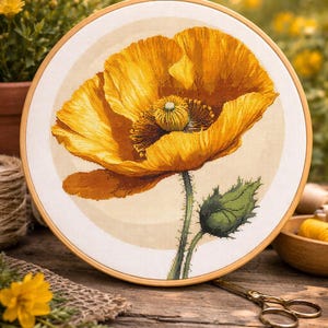 Puede incluir: Un bordado de punto de cruz de una amapola amarilla vibrante, enmarcado en un aro de madera. La flor tiene pétalos detallados y un tallo verde con una hoja. El fondo es de un color suave y neutro, y el aro se muestra sobre una superficie de madera.