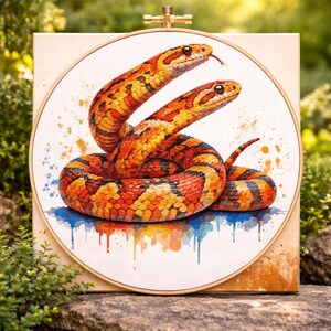 Könnte beinhalten: Kreuzstich-Kunstwerk mit zwei Schlangen in Orange-, Rot- und Gelbtönen, die sich umeinander winden. Die Schlangen haben detaillierte Schuppen und sind vor einem weißen Hintergrund mit farbigen Farbspritzern platziert. Das Kunstwerk ist in einem Holzreifen gerahmt.