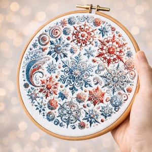 May include: A round embroidery hoop featuring a detailed cross-stitch design of snowflakes in shades of red, blue, and white. The snowflakes vary in size and style, creating a wintery scene. The embroidery is set in a wooden hoop.
