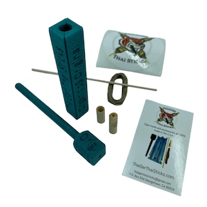 Może przedstawiać: Forma do cygar z tworzywa sztucznego w kolorze turkusowym z drewnianym kołkiem i szpulką sznurka. Forma ma oznaczenia dla różnych rozmiarów cygar. Opakowanie zawiera naklejkę z logo lisa i tekstem "Thai Sticks".