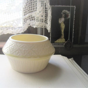 May include: A small, white ceramic bowl with a raised, embossed pattern. The bowl has a slightly rounded shape and a smooth, glossy finish.