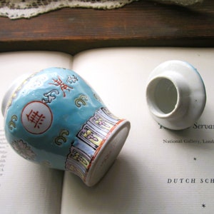 May include: A small, turquoise ceramic vase with a matching lid. The vase features Chinese characters and floral designs in red, yellow, and white. The lid is white with a blue rim.