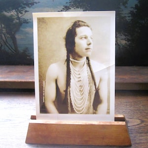 May include: A black and white photograph of a Native American man wearing a beaded necklace and a long braid. The photo is displayed in a wooden frame.