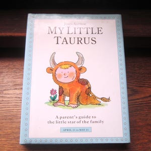 May include: A children's book titled "MY LITTLE TAURUS" by John Astrop. The cover features a cartoon illustration of a child in a bull costume. The book is a parent's guide to the little star of the family, with dates April 21 to May 21.