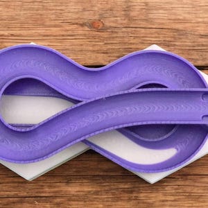 Może przedstawiać: Fioletowa plastikowa zabawka w kształcie ósemki, czyli toru nieskończoności, do kulek lub małych piłek. Tor ma fakturowaną powierzchnię.