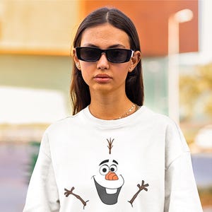 Puede incluir: Camiseta blanca con una imagen de dibujos animados de Olaf de la pel&iacute;cula Frozen. Olaf est&aacute; sonriendo con los brazos extendidos.