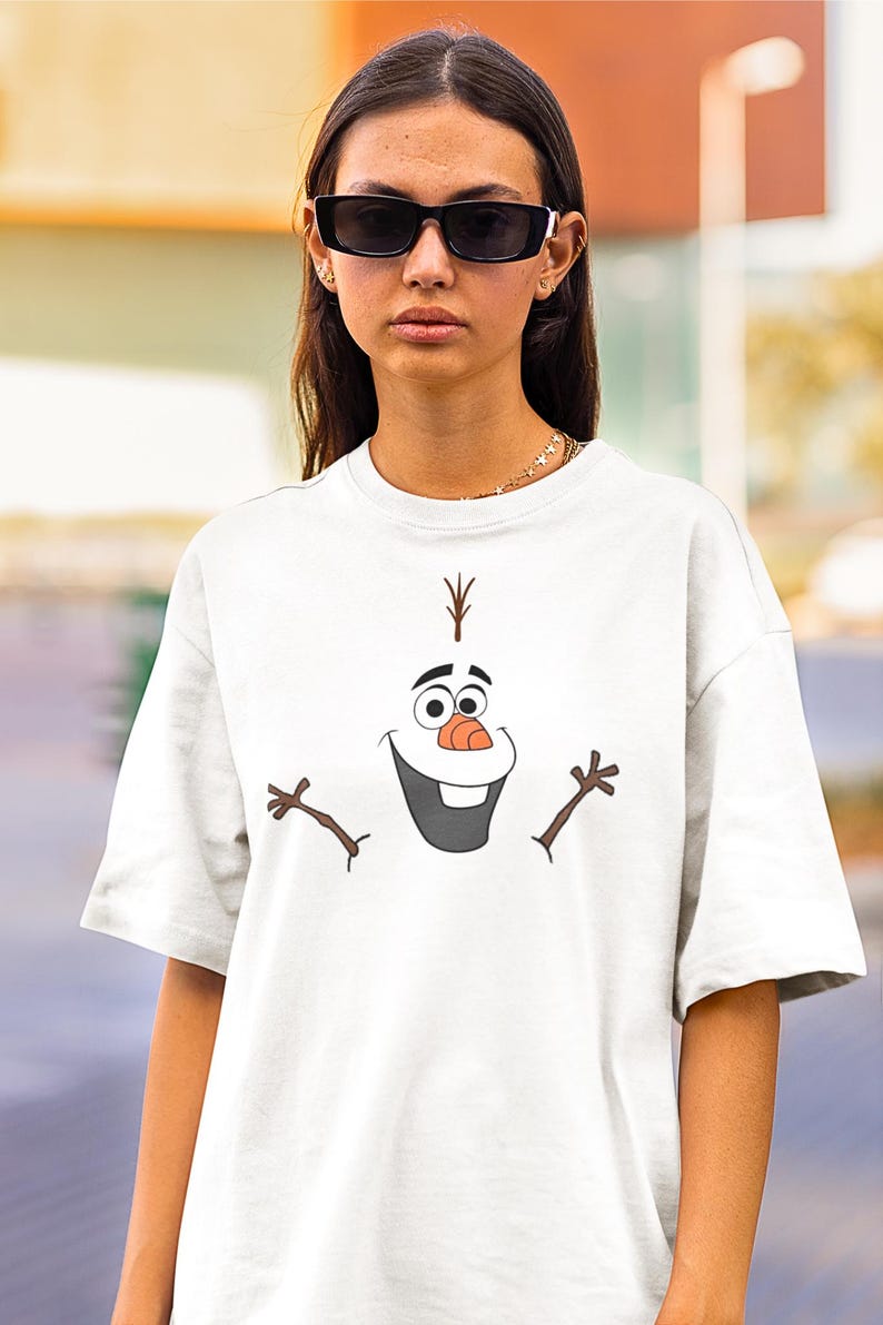 Puede incluir: Camiseta blanca con una imagen de dibujos animados de Olaf de la pel&iacute;cula Frozen. Olaf est&aacute; sonriendo con los brazos extendidos.