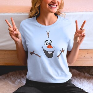 Puede incluir: Una camiseta azul claro con un gr&aacute;fico de Olaf de la pel&iacute;cula Frozen. Olaf est&aacute; sonriendo con los brazos extendidos.
