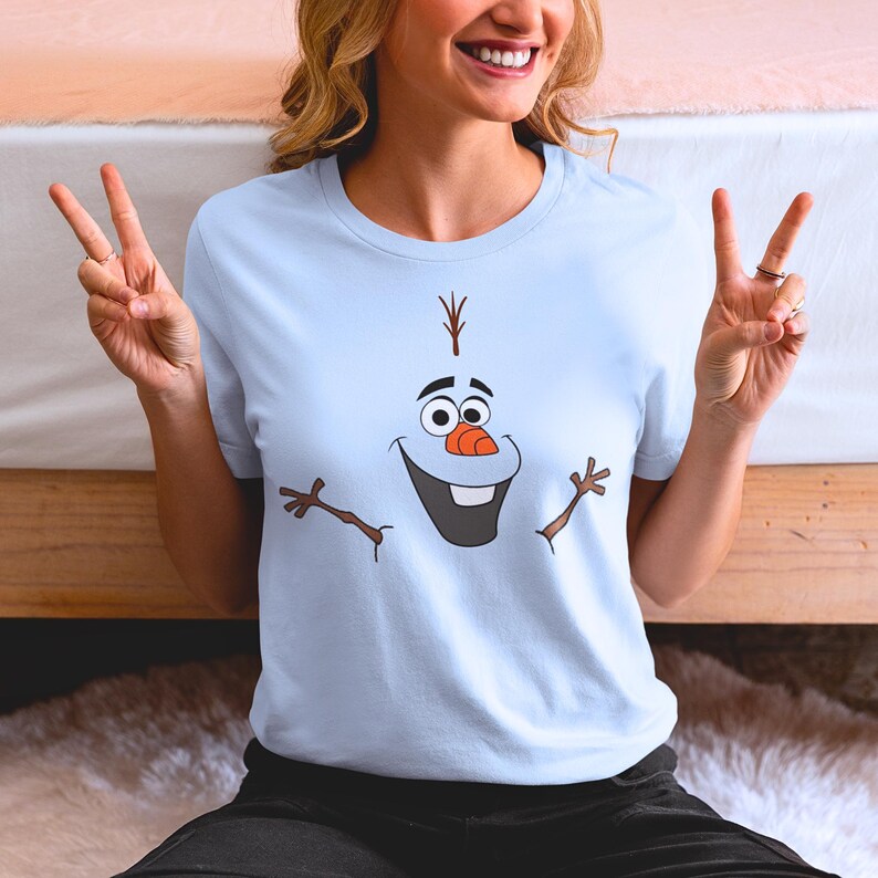 Puede incluir: Una camiseta azul claro con un gr&aacute;fico de Olaf de la pel&iacute;cula Frozen. Olaf est&aacute; sonriendo con los brazos extendidos.