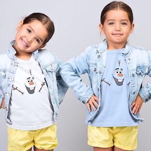 Puede incluir: Dos ni&ntilde;os con chaquetas vaqueras y camisetas a juego con un dibujo animado de Olaf de Frozen. La ni&ntilde;a de la izquierda lleva una camiseta blanca y la ni&ntilde;a de la derecha lleva una camiseta azul claro. Ambas ni&ntilde;as llevan pantalones cortos amarillos.