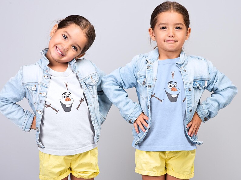 Puede incluir: Dos ni&ntilde;os con chaquetas vaqueras y camisetas a juego con un dibujo animado de Olaf de Frozen. La ni&ntilde;a de la izquierda lleva una camiseta blanca y la ni&ntilde;a de la derecha lleva una camiseta azul claro. Ambas ni&ntilde;as llevan pantalones cortos amarillos.
