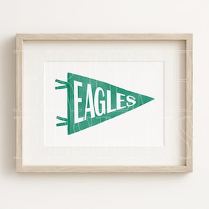 May include: A framed print featuring a green pennant with the word "EAGLES" in white block letters. The pennant is a triangle shape with a white background and a light wood frame.