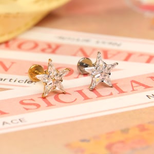 May include: Two star-shaped earrings with clear cubic zirconia stones. The earring on the left has a gold post, while the earring on the right has a silver post.