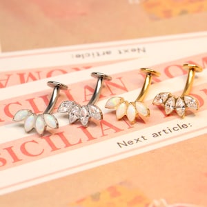 May include: Three surgical steel and gold body jewellery pieces with a curved barbell and a cluster of five opal-like stones. The stones are set in a prong setting and have a marquise shape.