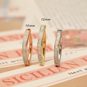 May include: Three hoop earrings with opal inlays. The earrings are in rose gold, gold, and silver tones. The sizes are 10mm and 12mm. The earrings are displayed on a printed background.
