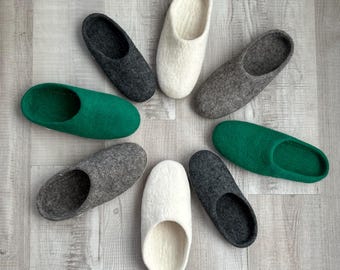 Puede incluir: Ocho pares de zapatillas de fieltro en una variedad de colores, incluyendo blanco, gris y verde. Las zapatillas están dispuestas en un círculo sobre un suelo de madera claro.
