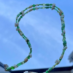May include: A green and white beaded necklace with a silver clasp. The necklace is made of small, round beads and is strung on a thin cord.