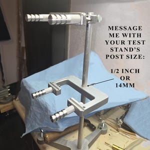 May include: A silver metal test stand featuring a vertical post and two horizontal arms with knurled cylindrical ends. Text on the image reads: MESSAGE ME WITH YOUR TEST STAND'S POST SIZE: 1/2 INCH OR 14MM. The stand has a stable base.