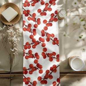 May include: White table runner with a repeating pattern of red berries on brown stems. The berries are round and clustered, creating a festive and natural design. The runner is made of a soft fabric and is suitable for a dining table or buffet.