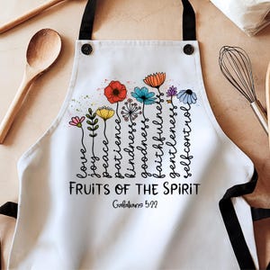 May include: White kitchen apron with a colorful floral design and the text "FRUITS OF THE SPIRIT Galatians 5:22".