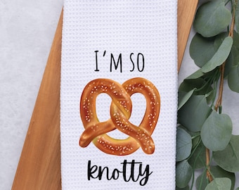 May include: White kitchen towel with a brown pretzel and the text "I'm so knotty" printed on it.