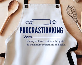 Könnte beinhalten: Weisse Schürze mit schwarzen Trägern. Auf der Schürze steht in Blau der Text "PROCRASTIBAKING" mit einer Nudelholz-Illustration. Der Text darunter definiert das Wort als Verb.