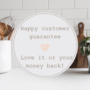 May include: White round sign with brown text that reads "Happy customer guarantee" with a pink heart in the middle and "Love it or your money back!" below the heart.