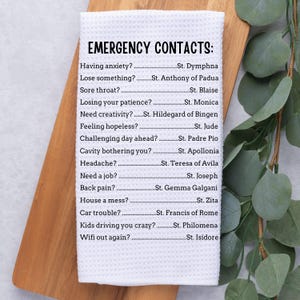 Puede incluir: Una toalla de cocina blanca con texto negro que enumera varias situaciones y los nombres de los santos correspondientes para obtener ayuda. El texto dice: "Contactos de emergencia: ¿Ansiedad? ... Santa Dymphna, ¿Perder algo? ... Santo Antonio de Padua, ¿Dolor de garganta? ... San Blas, ¿Perder la paciencia? ... Santa Mónica, ¿Necesitar creatividad? ... Santa Hildegarda de Bingen, ¿Sentirse desesperado? ... San Judas Tadeo, ¿Día desafiante por delante? ... San Padre Pío, ¿Problema dental? ... Santa Apolonia, ¿Dolor de cabeza? ... Santa Teresa de Ávila, ¿Necesitar un trabajo? ... San José, ¿Dolor de espalda? ... Santa Gemma Galgani, ¿Casa desordenada? ... Santa Zita, ¿Problemas con el coche? ... San Francisco de Asís, ¿Los niños te vuelven loco? ... Santa Filomena, ¿Wifi fuera de servicio? ... San Isidoro"