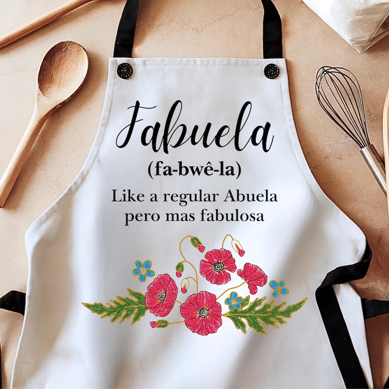 May include: White kitchen apron with black straps and a floral design. The apron has the text "Fabuela (fa-bw&ecirc;-la) Like a regular Abuela pero mas fabulosa" printed on it.
