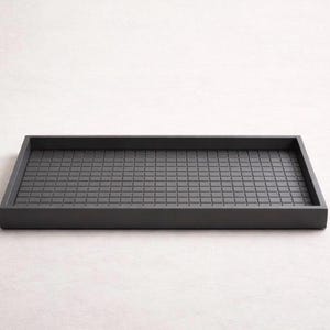 May include: A rectangular, dark gray tray with a grid pattern on the interior surface. The tray has a raised border and a matte finish. The design is simple and modern, suitable for serving or organizing items.