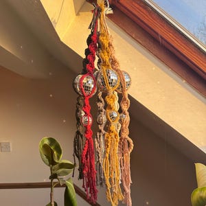 May include: Three macrame hanging ornaments with disco ball accents. The ornaments are red, brown, and yellow.