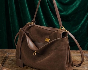 Könnte beinhalten: Eine dunkelbraune Wildlederhandtasche mit einem strukturierten Tragegriff und einem abnehmbaren Schulterriemen. Die Tasche verfügt über einen goldfarbenen Drehverschluss an der Frontklappe und ein kleines, rundes, goldfarbenes Zierelement.