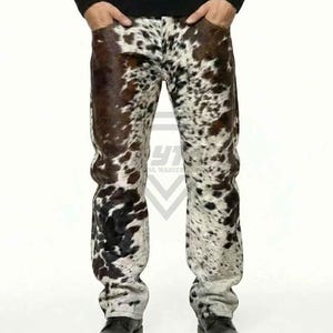 Peut inclure: Pantalon pleine longueur arborant un motif peau de vache distinctif avec un mélange de taches blanches, brunes et noires. Le pantalon présente une coupe droite, une ceinture standard avec passants et une braguette à boutons, avec une texture poilue.