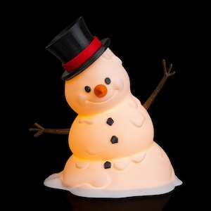 May include: A novelty snowman ornament with a black top hat and red band. The snowman has a carrot nose, black button eyes, and twig arms. The snowman is melting, with a warm, glowing light emanating from within.