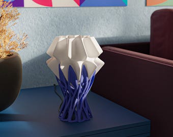May include: A contemporary table lamp featuring a white, geometric lampshade and a blue, branch-patterned base. The lamp is placed on a blue table. The design is modern and artistic, suitable for home decor. The lamp's design is contemporary and artistic.