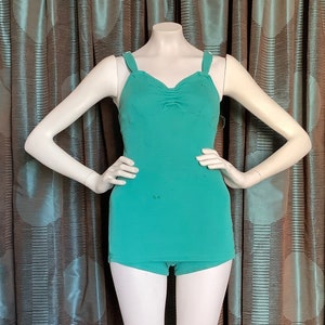 Pu&ograve; includere: Un costume da bagno intero color turchese con scollatura a cuore e spalline sottili. Il costume da bagno ha un dettaglio drappeggiato sul seno e uno stile a gamba corta a vita alta.