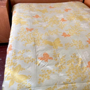May include: A bedspread with a light green background and a pattern of yellow and orange butterflies and floral elements. The bedspread is draped over a wooden bed frame.