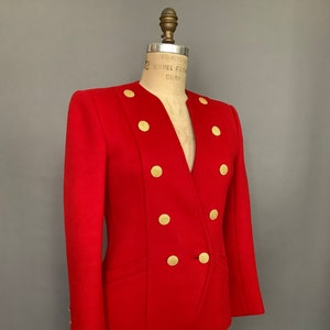 May include: A red blazer with gold buttons. The blazer has a v-neck and a double breasted closure.