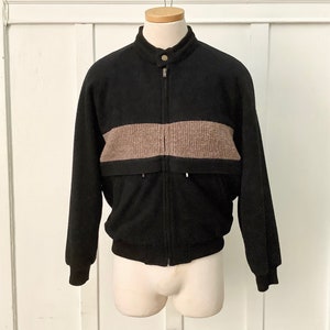 May include: A black zip-up jacket with a brown horizontal stripe across the chest. The jacket has a stand-up collar and a ribbed hem.