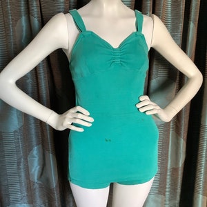 Pu&ograve; includere: Un costume da bagno intero color turchese con scollo a cuore e spalline sottili. Il costume da bagno ha un dettaglio drappeggiato sul seno e una silhouette aderente.
