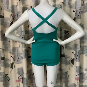 Pu&ograve; includere: Un costume da bagno blu turchese con un design a schiena incrociata. Il costume da bagno ha una scollatura rotonda e un taglio di gamba alto.